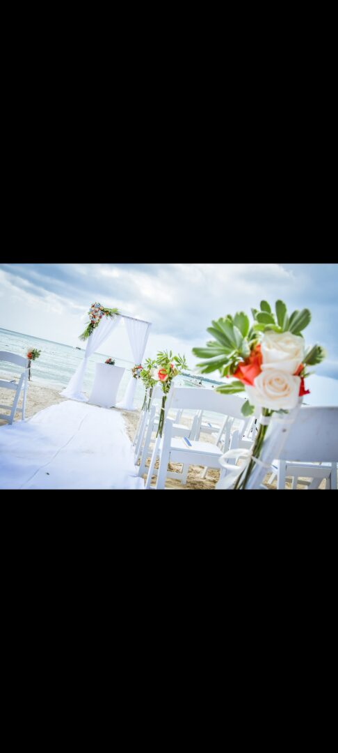 A wedding ceremony on the beach with white chairs.