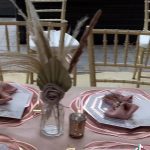 A table set with plates and napkins, a vase filled with feathers.