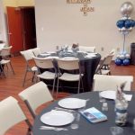 A room with tables and chairs, balloons and plates.