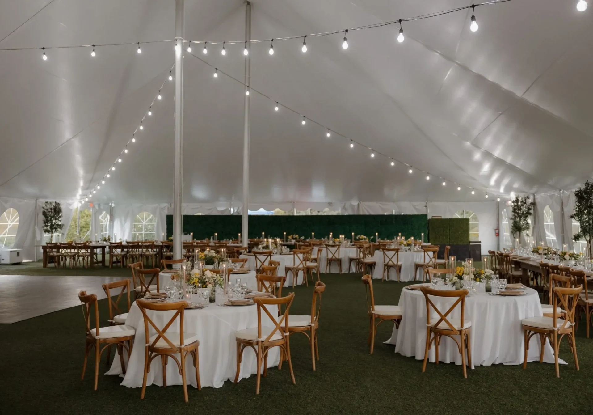 Elegant wedding reception setup under a large white tent with string lights.